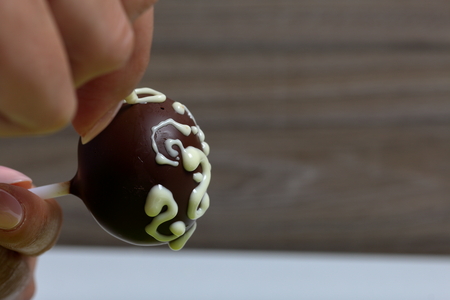 A woman decorates with the help of white chocolate popcake glazed with dark chocolate.