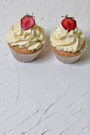 Cupcakes with strawberries and butter cream. On a white surface with decorative plaster.の写真素材