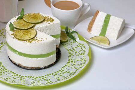 Lime cheesecake without baking. The piece is cut off. Lies on a plate. Near a cup of coffee with milk.の写真素材