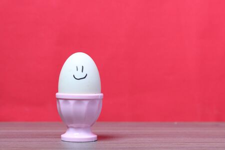 Boiled egg in poached pink. On the egg painted smiley. Against the background of coral color.の写真素材