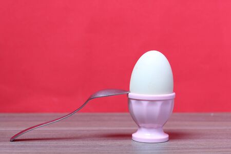 Boiled egg in poached pink. Next spoon for food. Against the background of coral color.