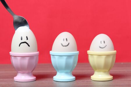 A boiled egg with a chopped shell stands in a poached. On the egg painted smiley. A spoon is stuck...