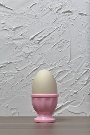Boiled egg in poached pink. Against the background of white wall with decorative plaster.