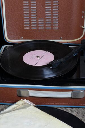 An old gramophone with a vinyl record mounted on it. Next to shabby paper envelopes are other...