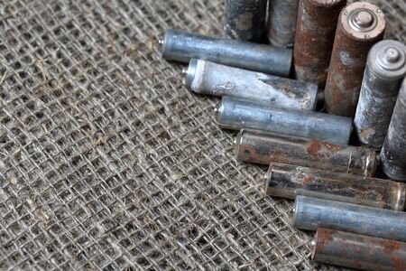 Spent batteries lie on a rough linen background. Covered with corrosion. Recycling and environmental...