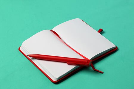 Notebook for notes in the red cover. With a red bookmark and pen. Lies opened on a mint background. School supplies.の写真素材