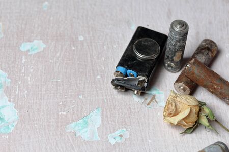 Spent batteries lie on the surface with peeling paint. Covered with corrosion. Nearby is a withered rose. Recycling and environmental protection.の写真素材
