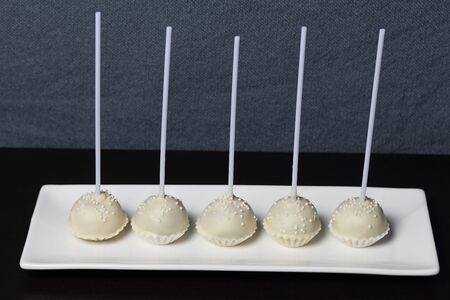 Cake pops in white chocolate glaze. Stand vertically on a stand. Decorated with white decorative sprinkles. On a gray background.の写真素材