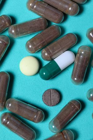 Gelatin pills and tablets of different colors. Medicines scattered on the background of mint color.の写真素材
