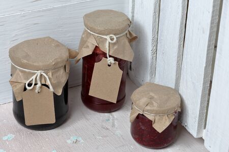 Jars of jam, covered with paper and tied with twine. On the string hang craft labels. On the background of wooden boards.の写真素材