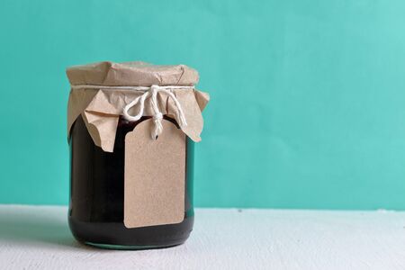 Jars of jam, covered with paper and tied with twine. On the string hang craft labels. Against the background of mint color.の写真素材