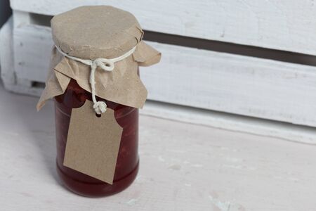 Jars of jam, covered with paper and tied with twine. On the string hang craft labels. On the background of wooden boards.の写真素材