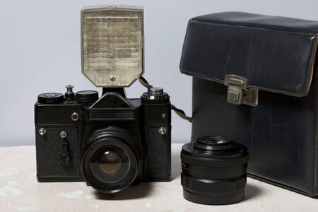 Old film camera, removable lens and wired flash. They lie on the surface of the table.