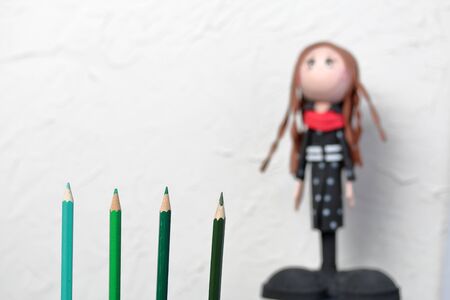 Color pencils in green shades. They are located vertically. Against the background of a white wall with decorative plaster. The figure of a schoolgirl is out of focus.の写真素材