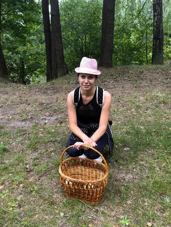 Satisfied woman mushroom picker with a hat on her head and a backpack over her shoulders. I sat down at a basket for picking mushrooms in a forest glade.の写真素材