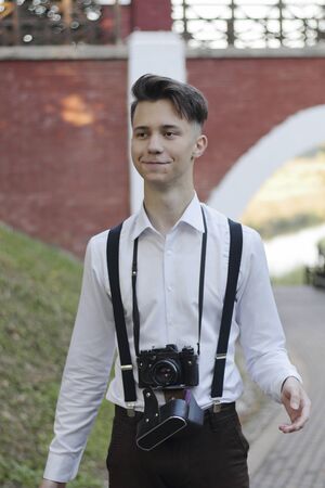 Stylishly dressed young man is walking in the park. In his hands holds a SLR film camera.