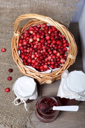 Homemade preserves, cranberry jam in jars. One can is open, it has a teaspoon. Several berries are scattered on the surface.の写真素材