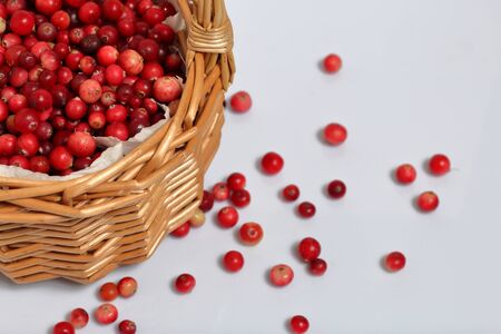 Basket filled with cranberries. It stands on a surface covered with linen cloth. Several berries are scattered on the surface.の写真素材