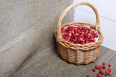 Basket filled with cranberries. It stands on a surface covered with linen cloth. Several berries are scattered on the surface.の写真素材