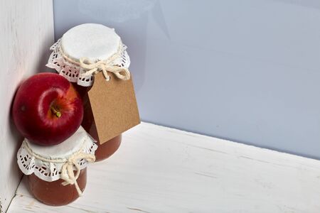 Homemade seasonal preparations. Beautifully packaged jars of apple jam. Covered with paper and tied with a cord. Nearby are fresh apples.の写真素材