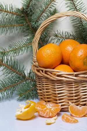 Tangerines in a wicker basket. Next to the basket is peeled mandarin. Visible slices of mandarin and skin from it. Branches of green spruce. On white background.の写真素材