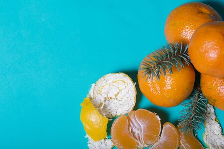 Tangerines are stacked in a pyramid. Next to them is peeled mandarin. Visible slices of mandarin and skin from it. A branch of blue spruce. On a mint background.の写真素材