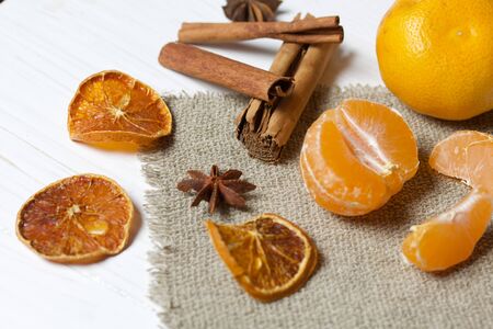 Tangerines, anise and cinnamon sticks. Nearby are slices of dried mandarins. Lying on a piece of linen. Against the background of white painted boards.の写真素材