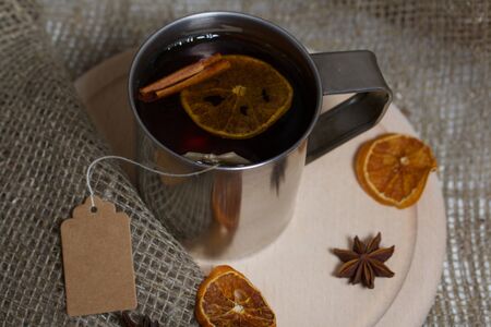 Brewed tea bag in a metal mug. A slice of dried mandarin floats in it. Nearby peeled mandarin, anise stars and cinnamon sticks.の写真素材