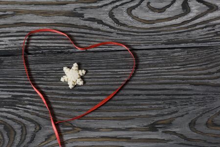 Snowflakes from pastille in the center of a scarlet ribbon laid in the shape of a heart. On old pine boards painted black.の写真素材