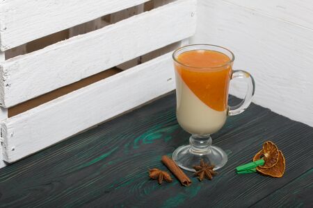 Two layers of jelly in glass goblets. Cream and tangerine jelly. Nearby are spices for decoration. On the surface of brushed boards painted black and green.の写真素材