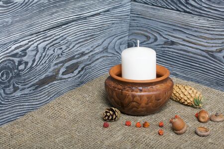 A large candle in a clay vessel. Acorns and rowan berries are scattered nearby. Against the background of brushed boards.の写真素材