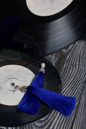 Homemade tassel earrings in blue. Against the background of old vinyl records and brushed pine boards painted in black and white.の写真素材