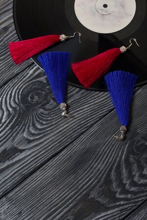 Homemade earrings tassels of red and blue. Against the background of old vinyl records and brushed pine boards painted in black and white.の写真素材
