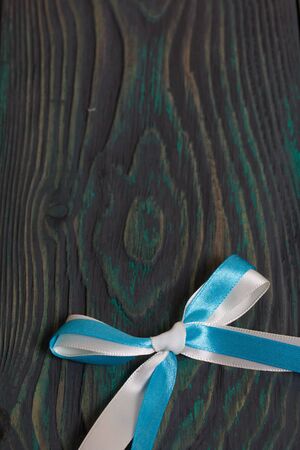 Two ribbons of different colors tied to a bow. Lies on pine brushed boards painted in black and green.の写真素材