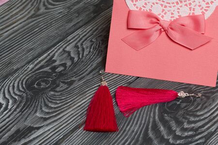 Homemade red tassel earrings and a greeting card. They lie on brushed pine boards painted in black and white.の写真素材