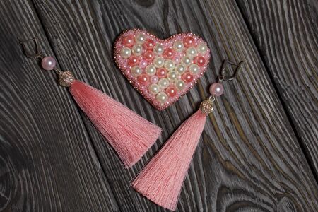 Heart bead brooch. Earrings tassels pink. On brushed pine boards painted in black and white.の写真素材