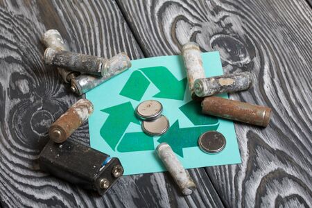Spent finger-type batteries coated with corrosion. Waste recycling sign. They lie on brushed pine boards painted in black and white.の写真素材