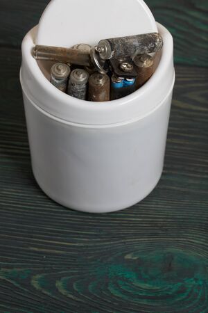 Waste bin. It contains finger-type batteries coated with corrosion. Against the background of brushed pine boards painted in black and green.の写真素材
