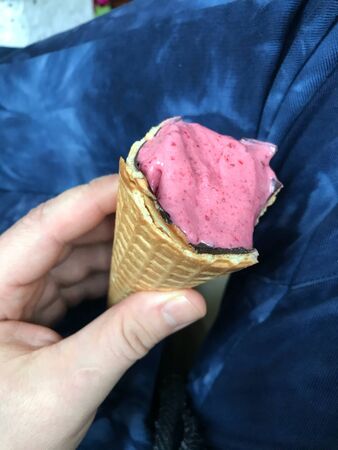 Strawberry ice cream in a waffle cone. In a manâ€™s hand. Against the background of male legs...