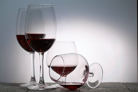 Glasses with red dry wine. One of them lies on its side with the remains of wine. Stand on wooden boards. Shot in backlight.の写真素材
