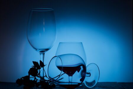 Glasses with red dry wine. One of them lies on its side with the remains of wine. Dried rose...