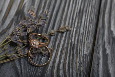 Wedding rings lie next to a bouquet of lavender. On brushed pine boards painted in black and white.