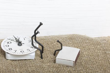 Figurines of man made from carpentry nails. They are sitting on the watch dial, next to each other....