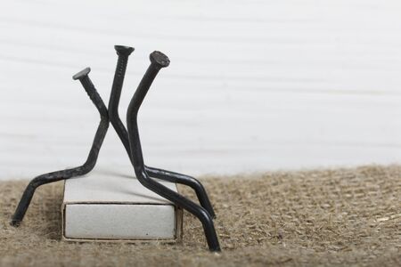 Figurines of man made of carpentry nails. They sit on a box of matches, their backs to each other.の写真素材