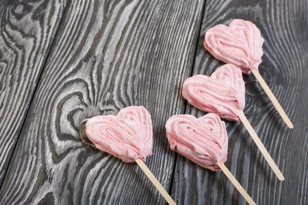 Delicate pink marshmallows in the shape of a heart on a stick. Several pieces lie on brushed pine boards painted in black and white.の写真素材