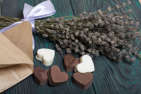 An open white paper bag on brushed pine boards. Chocolate hearts are scattered from it. From white and black chocolate. Near a bouquet of lavender.の写真素材