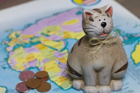 A ceramic piggy bank with a slot for coins is on the world map. Several coins are scattered nearby. Piggy bank for travel.の写真素材