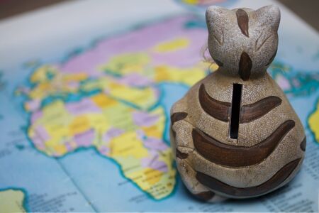 A ceramic piggy bank with a slot for coins is on the world map. Piggy bank for travel.の写真素材