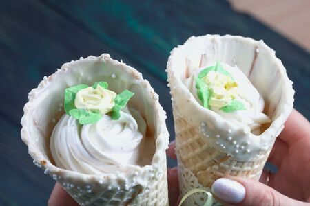 A woman holds in her hand two waffle cones with marshmallows. They are decorated with white...