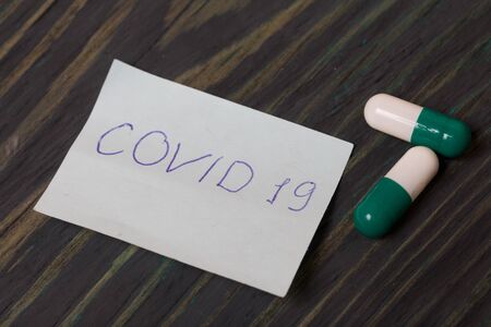 Paper sticker with the inscription COVID-19. Nearby are several pills of white-green color. Lying on brushed pine boards.の写真素材
